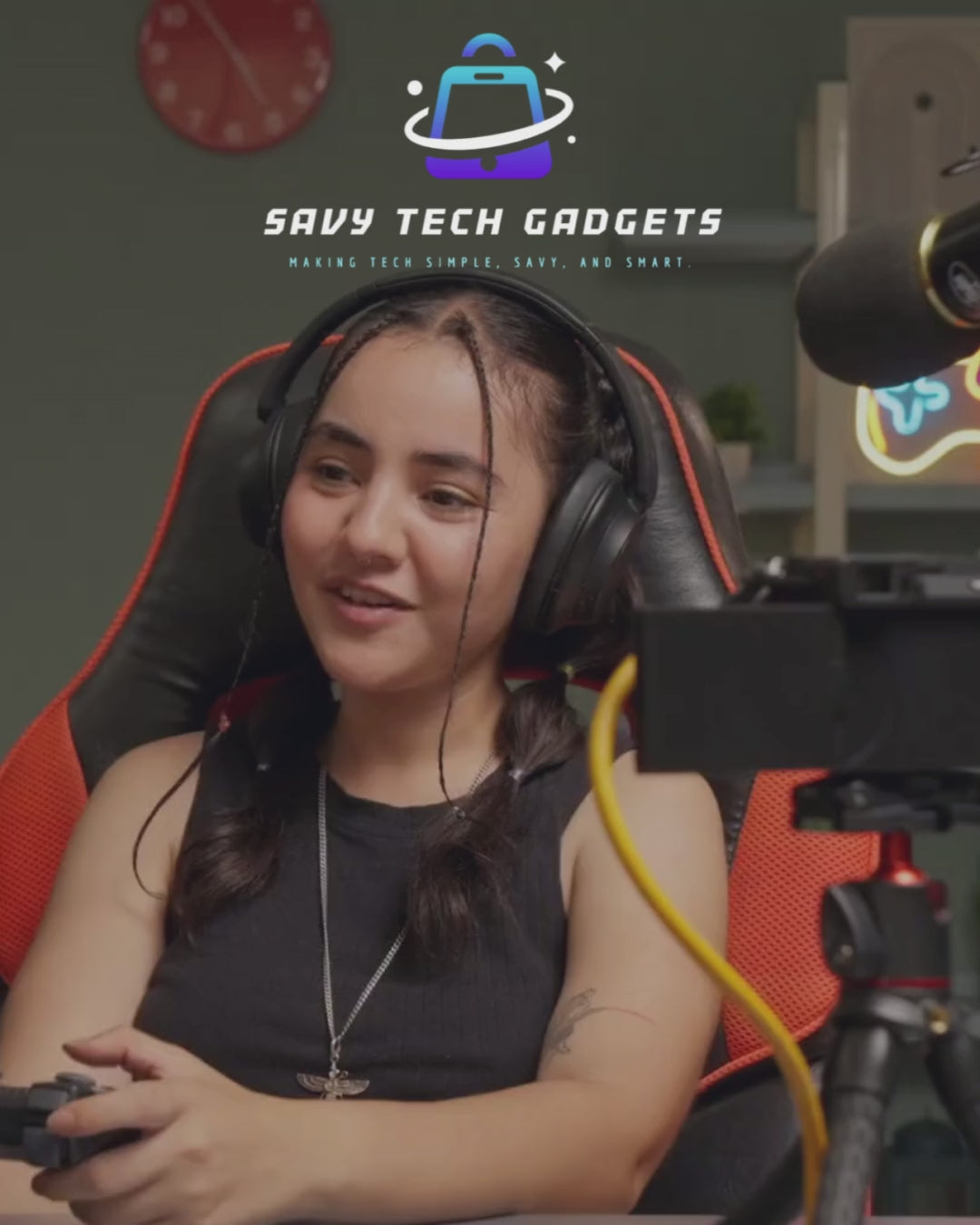 Load video: savy tech gadgets logo with gamer girl happy playing on controller with products behind and microphone and camera in front, wearing great headphones